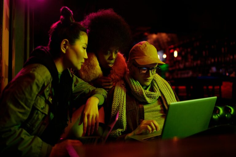 Group of diverse young adults working together on a laptop in a dimly lit bar setting.